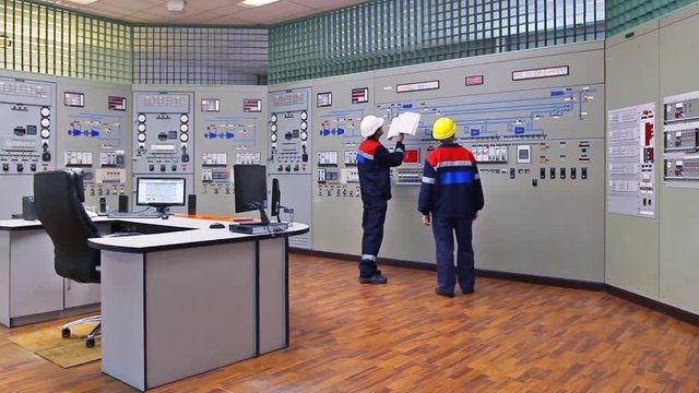 two engineers talk while showing examples on circuit at main control panel of gas compressor station