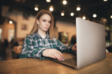 Background. Woman sits in a cafe with a laptop, listens to music in the headphones and works. Lady with a laptop in a cozy coffee shop. Focus on the laptop and the girl's hand. Abstract blurred photo