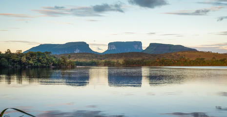 The sun sets over three small mountains across from a river in Ucaima. Canaima National Park, Venezuela