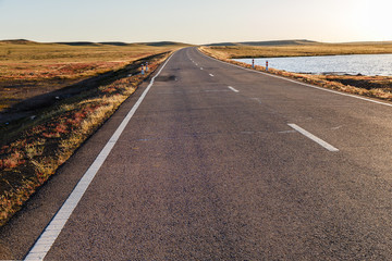 Asphalt road in Mongolian steppe along a small lake, Mongolia