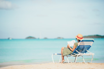 Young woman reading book on chaise-lounge on the beach