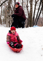 A little girl (3 yr old) sledging in Quebec, while mum looks on