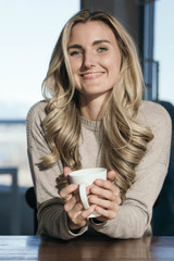 Blonde girl drinking coffee tea or soup from a white mug