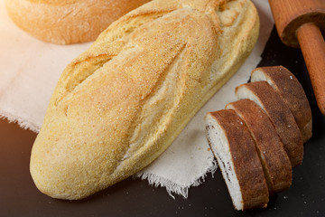 Bakery - rustic crusty loaves of bread and rolling pin on black chalkboard background. Still life captured from above. Layout with free copy space.