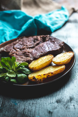 home-made dinner, roast beef steak with baked potatoes and butter and fresh leaves of field salad, on a dark wooden kitchen table