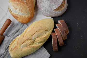 Bakery - gold rustic crusty loaves of bread and rolling pin on black chalkboard background. Flat lay, top view, copy space for your text