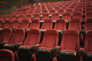 Empty cinema. Rows of comfortable red chairs towards to big screen in illuminate red room cinema. Mock Up.