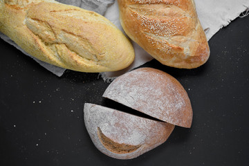 Bakery - gold rustic crusty loaves of bread on black chalkboard background. Flat lay, top view, copy space for your text
