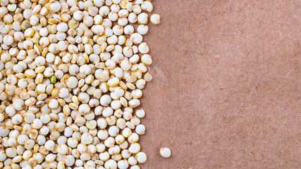 Seeds of uncooked Chenopodium quinoa, source of protein for vegetarians on brown natural paper background, Macro shot with copy space for text and design