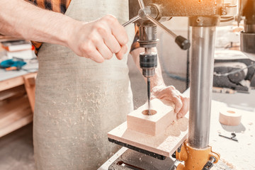 Close-up of a joiner hands working with wood on a lathe drilling machine at the factory. Carpenter...