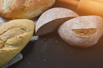 Bakery - gold rustic crusty loaves of bread and rolling pin on black chalkboard background. Flat lay, top view, copy space for your text