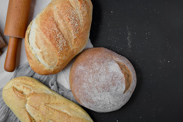 Bakery - gold rustic crusty loaves of bread and rolling pin on black chalkboard background. Flat lay, top view, copy space for your text