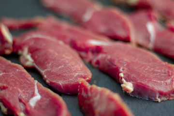 Red pieces of fresh veal, sliced on raw thin beef steaks, laid out on a black stone slate. The recipe for cooking meat steaks. High definition photos. Raw beef for steaks.