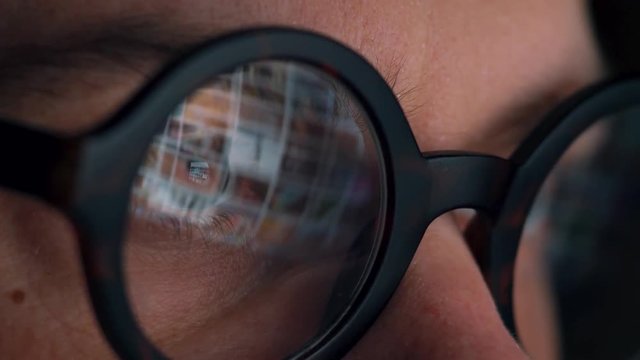 Man in glasses looking on the monitor and surfing Internet. The monitor screen is reflected in the glasses