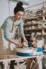 Attractive young lady in apron working on pottery wheel