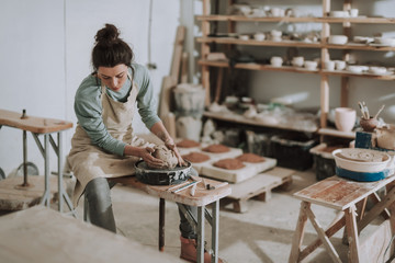 Beautiful young lady in apron working in pottery workshop