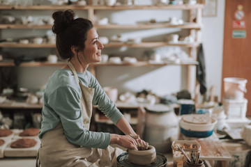 Joyful young lady in apron working on pottery wheel