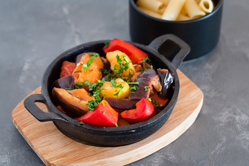 Vegetarian ratatouille with baked aubergine, zucchini, pepper in tomato sauce. Dish served with pasta.