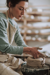 Beautiful brunette lady in apron working on pottery wheel