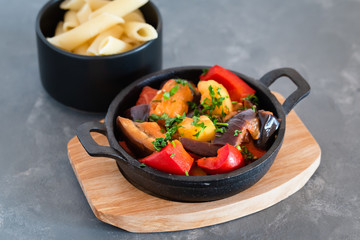 Vegetarian ratatouille with baked aubergine, zucchini, pepper in tomato sauce. Dish served with pasta.