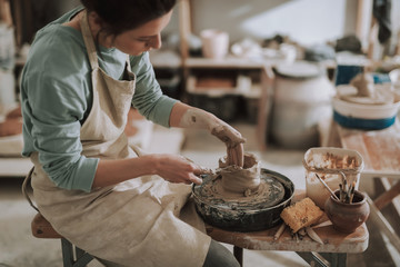 Female ceramic artist using sculpture scraper knife while making clay pot