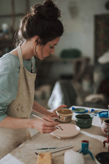 Charming young woman in apron working in pottery workshop