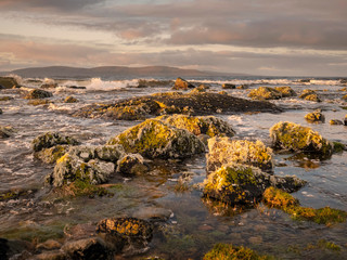 Obraz premium West coast of Ireland, Galway bay shore line, rocks, waves, Burren mountains in the background. Dramatic sky.