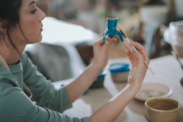 Young woman painting candleholder in blue color at workshop