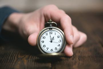 Man is holding in hand a pocket watch on a brown table background.