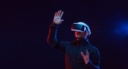 Model young man with beard in glasses of virtual reality on dark background.. Augmented reality, science, future technology concept. VR. Futuristic 3d glasses with virtual projection. Neon light.