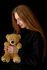 Teenage girl with a teddy bear on a black background.