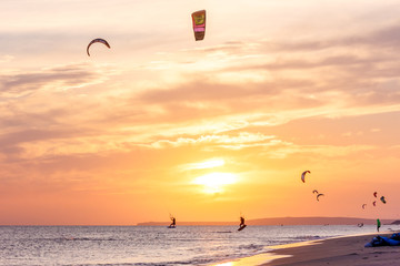 extreme group of professional kiters slide waves, jumps air on black sea with sail wing in hands led wind an sunset, onlookers photographers seagull on shore. village of annunciation. backlit, toned
