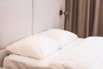 Fototapeta na wymiar Bed in a bedroom with white linen, pillows and a blanket close up, sconces on the wall