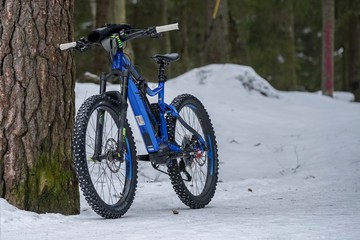 Fototapeta na wymiar Helsinki, Finland - March 13, 2019: Electric mountain bike standing against tree on snowy ground in Helsinki