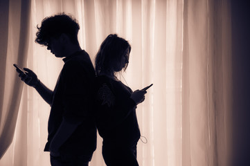 Silhouette of two teenagers with cell phones standing back to back, brown effect - 258613917