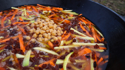 Uzbek national dish pilaf in a large cast-iron cauldron on the fire