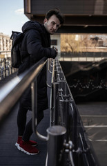 Fototapeta na wymiar Handsome stylish man model posing on the bridge near buildings. City style