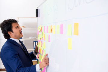 Young handsome employee in front of whiteboard with to-do list  
