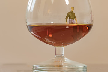 Miniature man figure sinking in the glass of brandy. Shallow depth of field background. Healthcare and alcoholism concept.