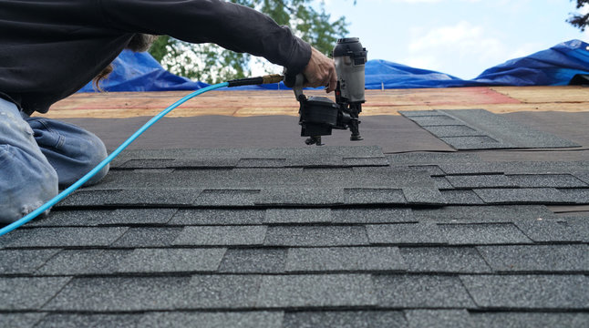 Handyman Using Nail Gun To Install Shingle To Repair Roof