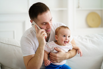 young father teleworking, talking on mobile phone and babysitting. Working dad and cute baby son in living room. parenting, family, freelance and childcare