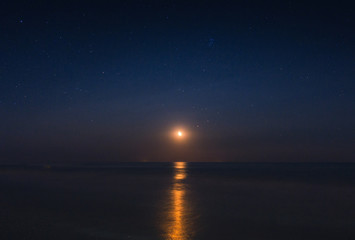 Fototapeta na wymiar Full moon reflected in the starry night in the waves of the sea