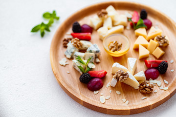 Assortment of different cheese types on wooden platter. slices of cheese camembert with parmesan, dorblu and maasdam served with walnuts and honey