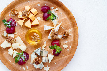 cheese plate. banquet, restaurant menu. slices of various cheeses. camembert, parmesan, dorblu  and maasdam served with grapes, walnuts and honey on wooden board