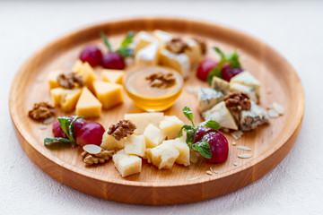 Different kinds of cheeses with grapes, walnuts and honey on wooden platter. gourmet food, delicious appetizer, banquet