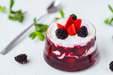 Layered berry dessert trifle in small portioned glass jar. Sponge cake and fresh berries covered with tasty whipped cream