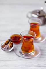 Glass cups of aromatic black tea, teapot and sweets on white table background