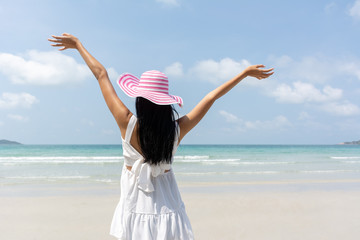 Beautiful young Asian woman wear hat happy stand on sand of the sea and show hand in to sky relaxing on beach on summer holidays vacations. Concept freedom, Lifestyle, tourism, holiday.