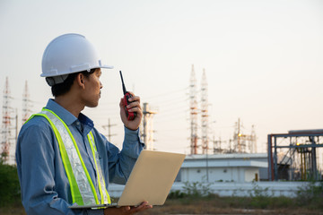 Engineers male working with laptop and operate the radio for workers security control at power plant. Energy power station area with sky, sunset. Concept safety,industry