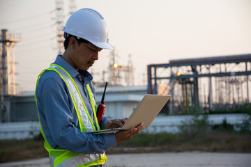 Engineers male working with laptop for workers security control at power plant. Energy power station area with sky, sunset. Concept safety,industry